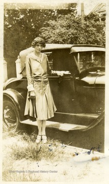 African-American student, Anna Frazier, poses next to an early automobile.
