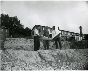 Two men and President Richard McKinney (right) look at blue prints for a student construction project.