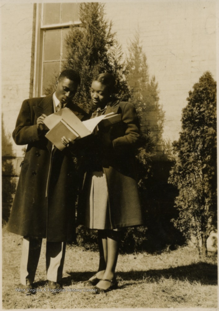 A male and female student stand outside looking at papers in a file together.