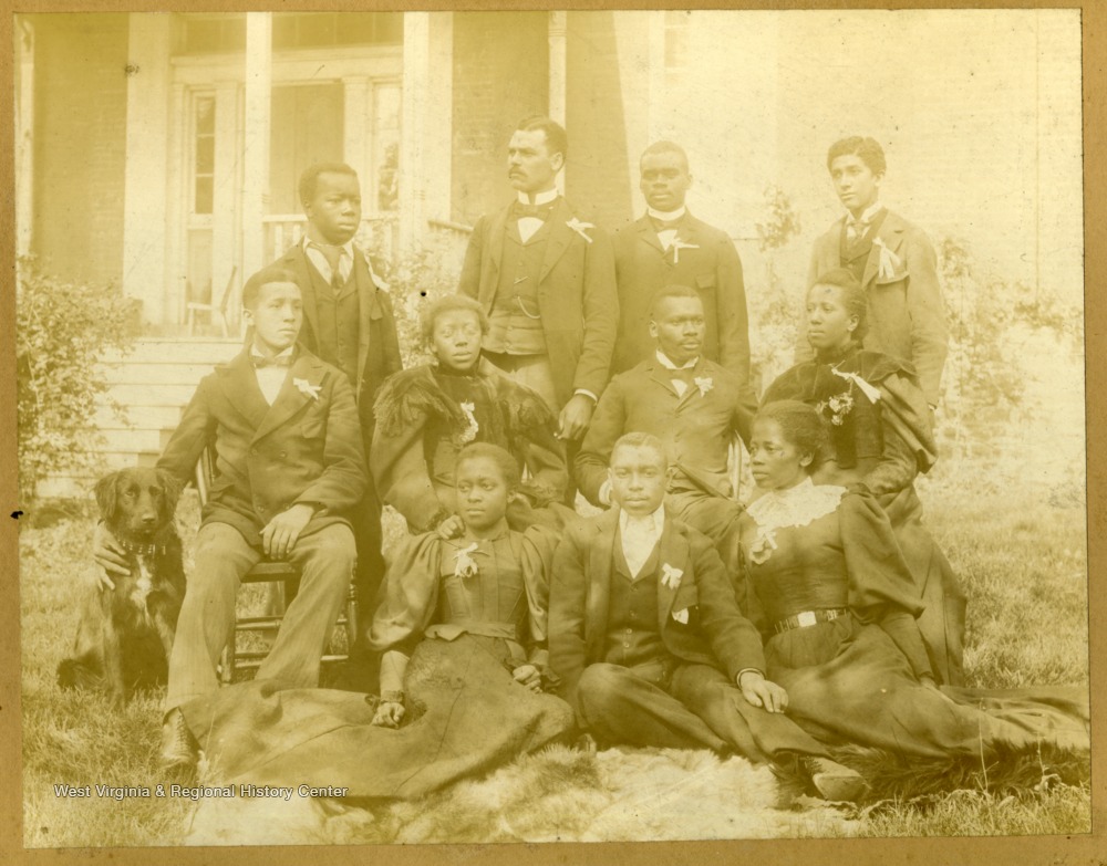 Group shot of Storer College students sitting and standing on lawn with dog.