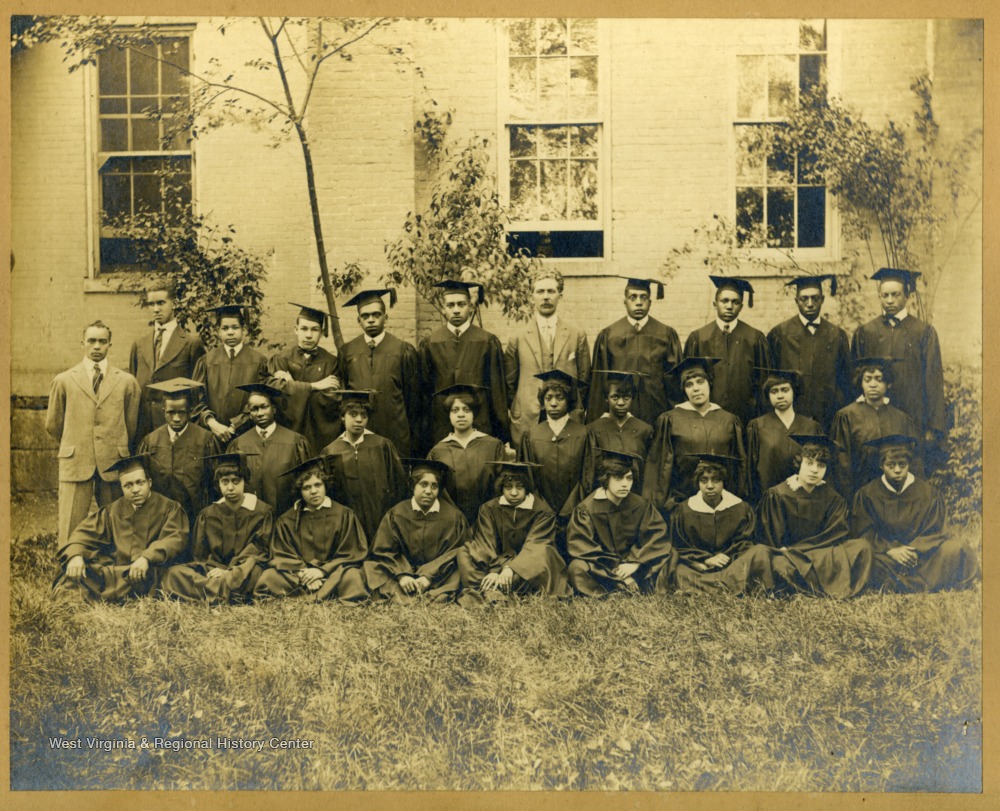 Group shot of graduating class in caps and gowns in front of building on Storer College Campus. Pres. McDonald in middle.