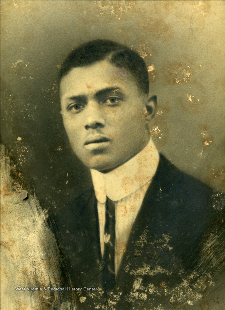 A young African American man, possibly a student, in a suit  wearing "ARROW"-style collar and thin tie.