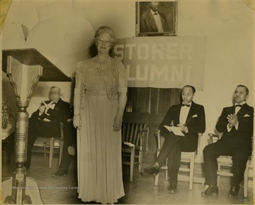 Woman in dress stands in foreground.