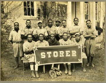 Storer College baseball team in uniform in front of building. Front row holding "STORER" banner.
